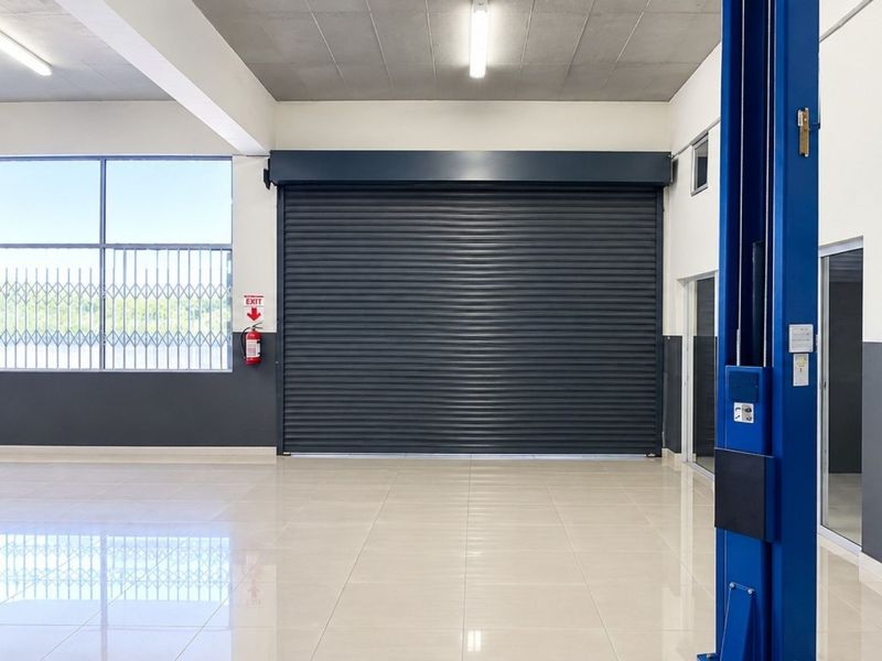 Spacious commercial garage featuring a large roller shutter door, integrated vehicle lift, polished tiled flooring, and secure glass access points.