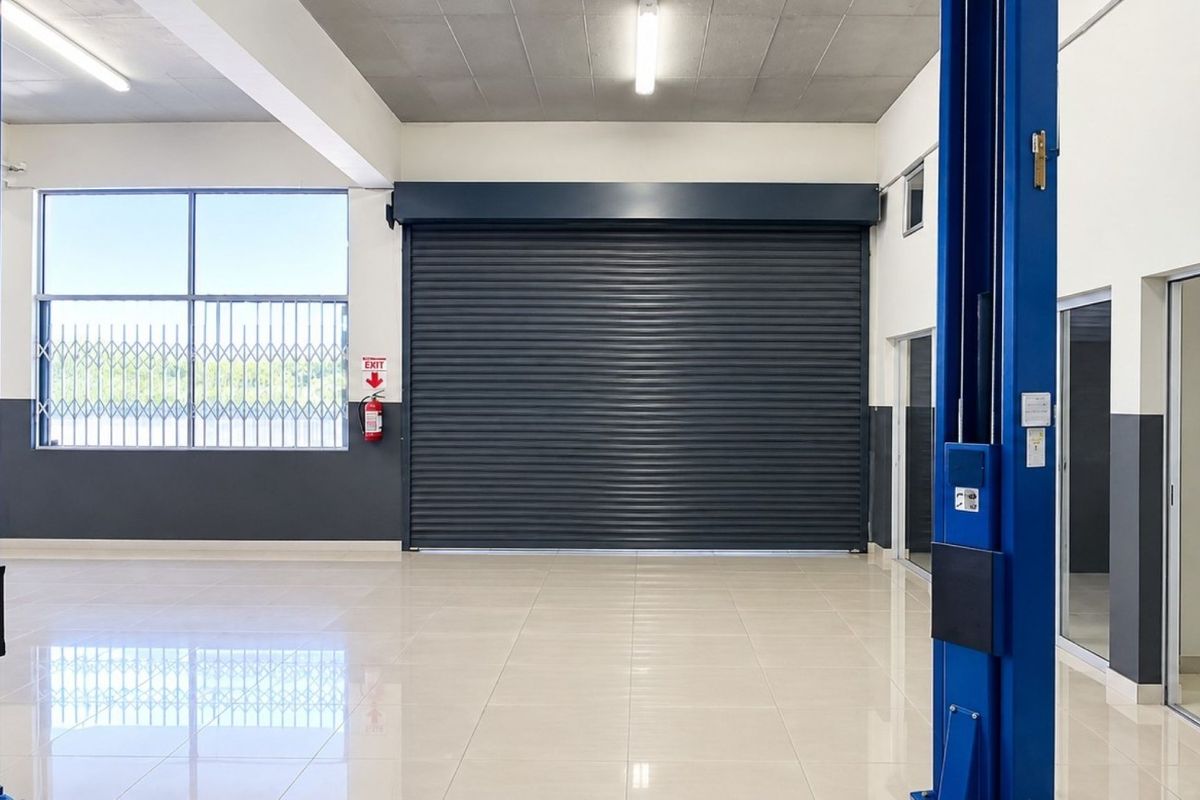 Spacious commercial garage featuring a large roller shutter door, integrated vehicle lift, polished tiled flooring, and secure glass access points.