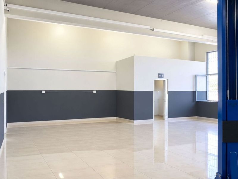 Spacious commercial utility area featuring polished tile flooring, high ceilings, security bars on windows, and an integrated automotive lift system.