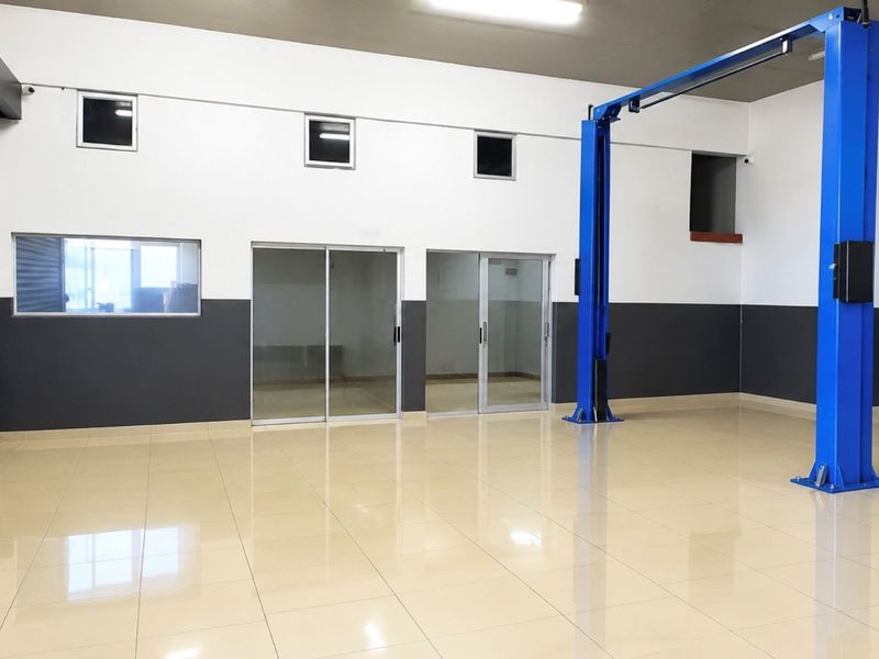 Spacious commercial garage featuring polished tiled flooring, a professional two-post vehicle lift, and secure roller shutter access.