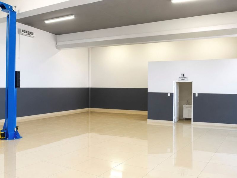 Spacious commercial garage featuring high-gloss tiled flooring, a built-in vehicle hoist, modern lighting, and an integrated customer restroom.