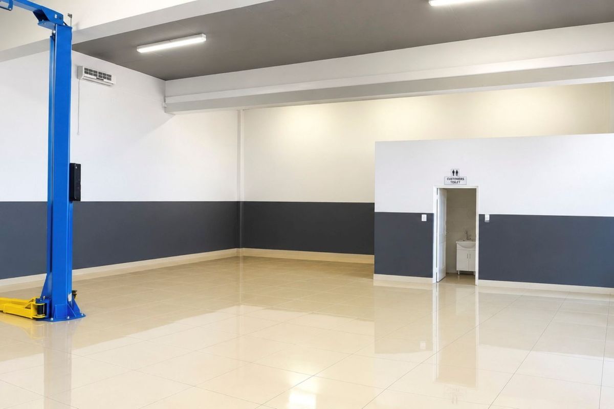 Spacious commercial garage featuring high-gloss tiled flooring, a built-in vehicle hoist, modern lighting, and an integrated customer restroom.