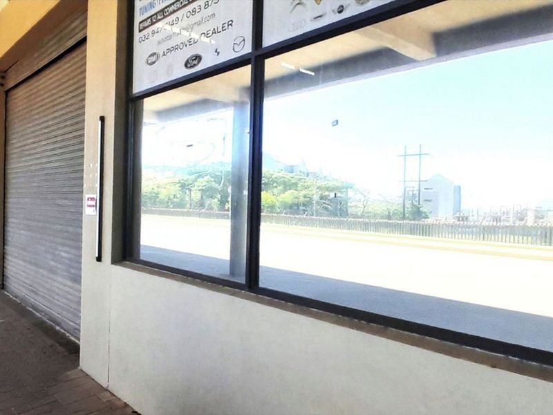 Commercial storefront featuring a large display window, roller shutter door, and paved walkway, suitable for retail or showroom use.