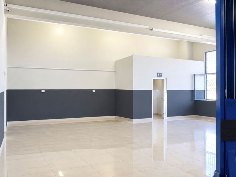 Spacious commercial utility area featuring polished tile flooring, secure window bars, and an integrated vehicle lift, suitable for workshop or automotive use.