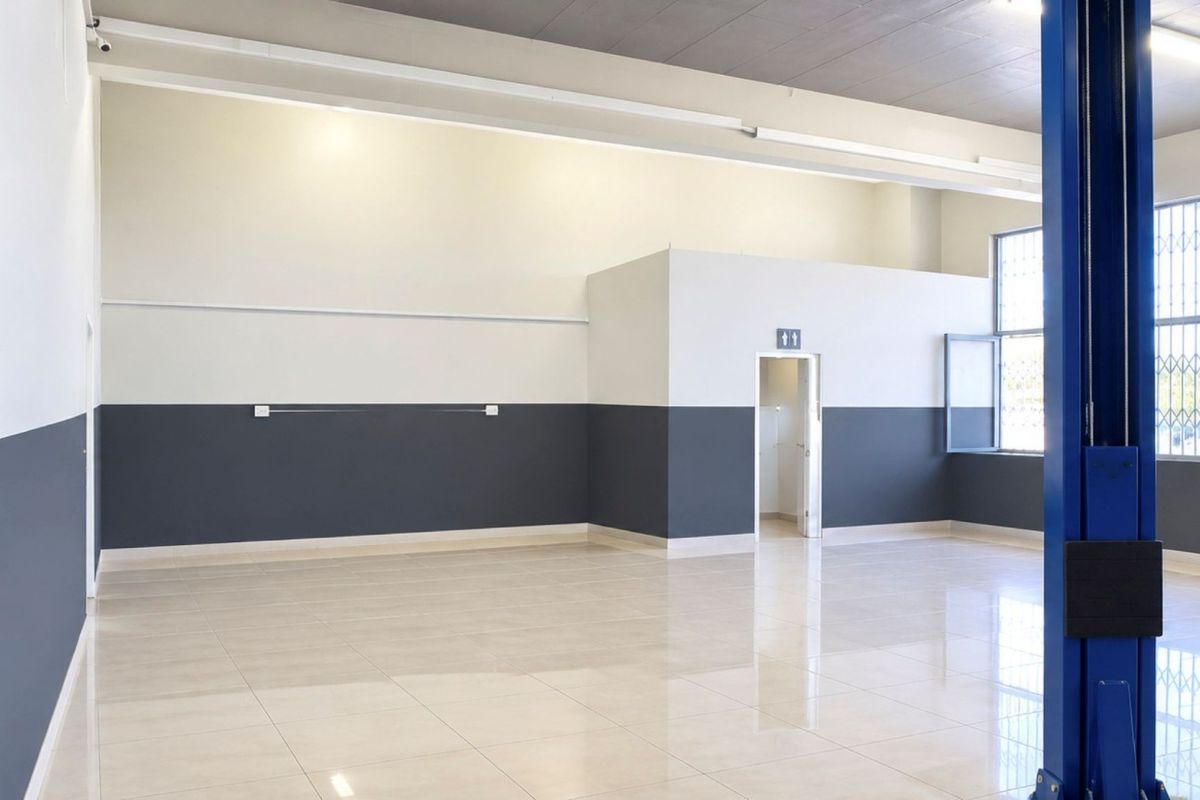 Spacious commercial utility area featuring polished tile flooring, secure window bars, and an integrated vehicle lift, suitable for workshop or automotive use.