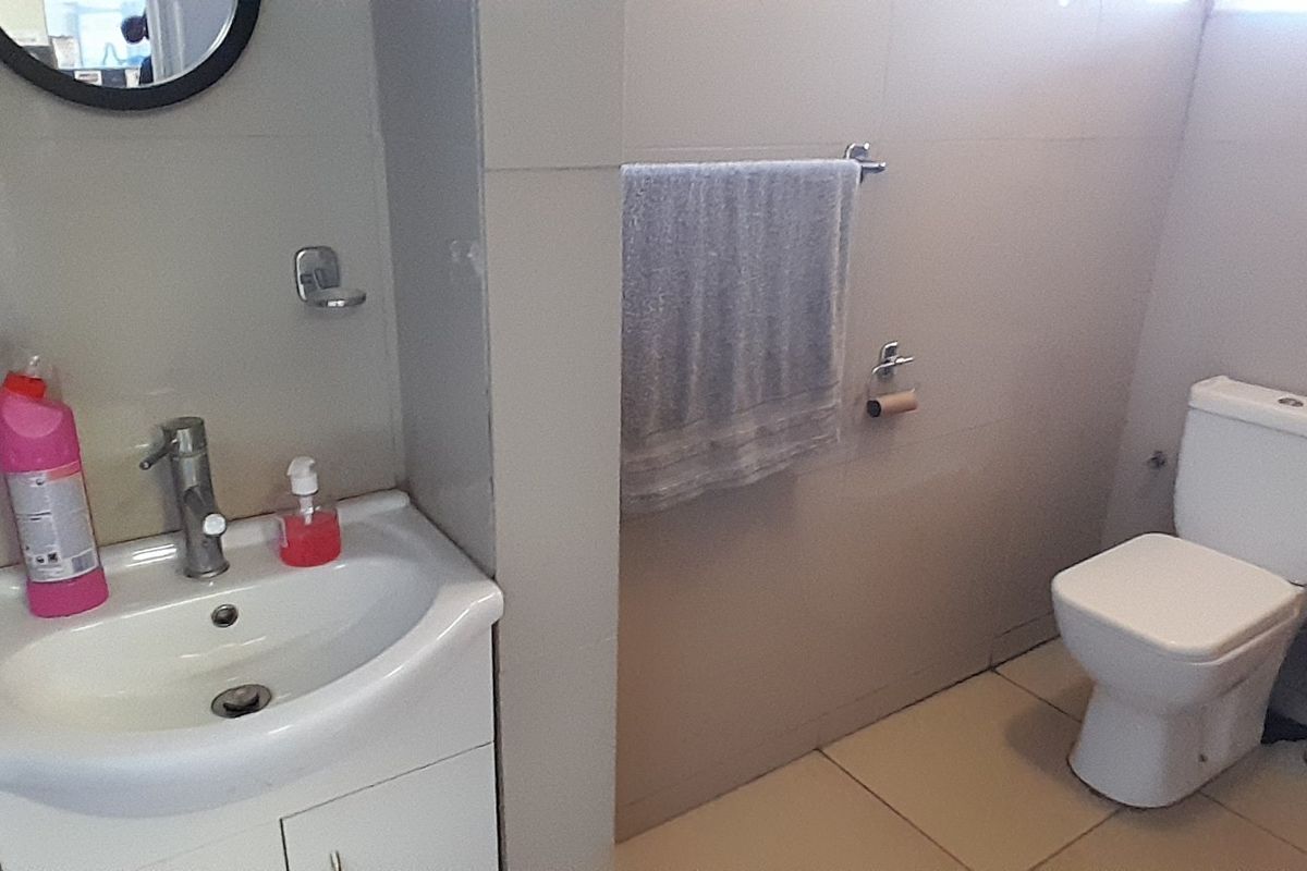 A functional bathroom featuring a vanity basin with mixer tap, a standard toilet, and neutral wall and floor tiling.