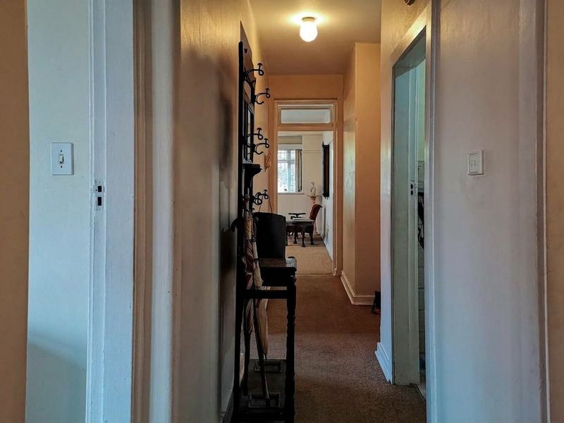 A narrow residential hallway connecting multiple rooms, featuring carpeted flooring and standard door frames, requiring cosmetic updates to improve the overall aesthetic.