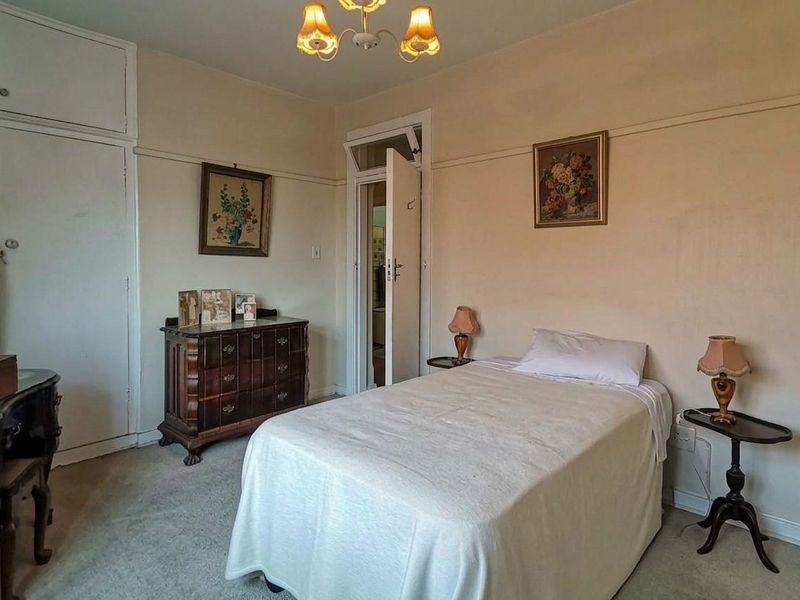 A bedroom featuring built-in wardrobe storage, a picture rail, and a transom window above the door, offering a classic layout with potential for modernization.