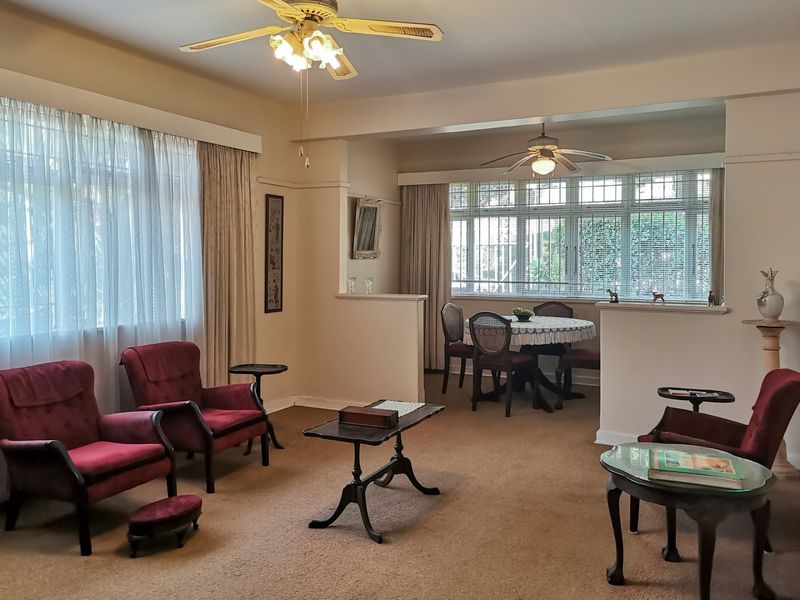 Spacious open-plan living and dining area featuring large windows, ceiling fans, and a half-wall partition creating distinct zones.