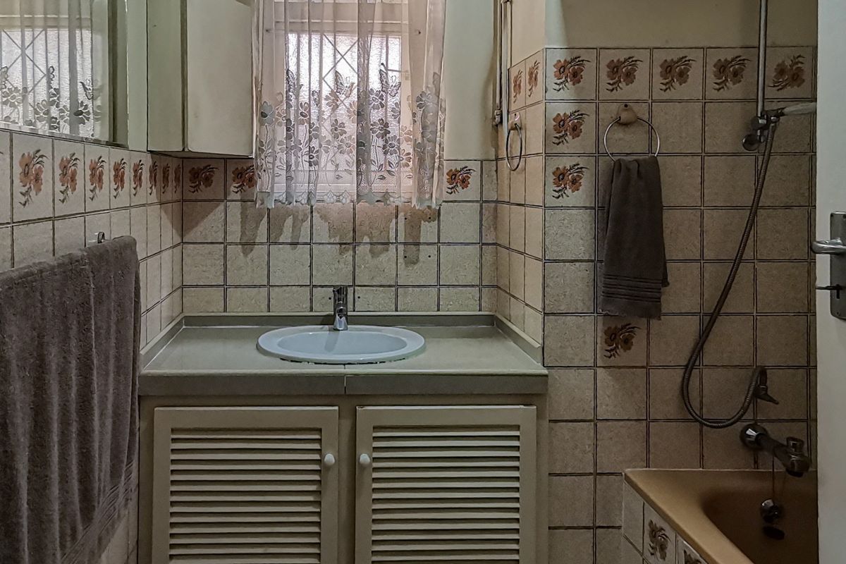 A dated bathroom featuring a vanity cabinet with a drop-in basin, wall tiles, and shower fixtures.