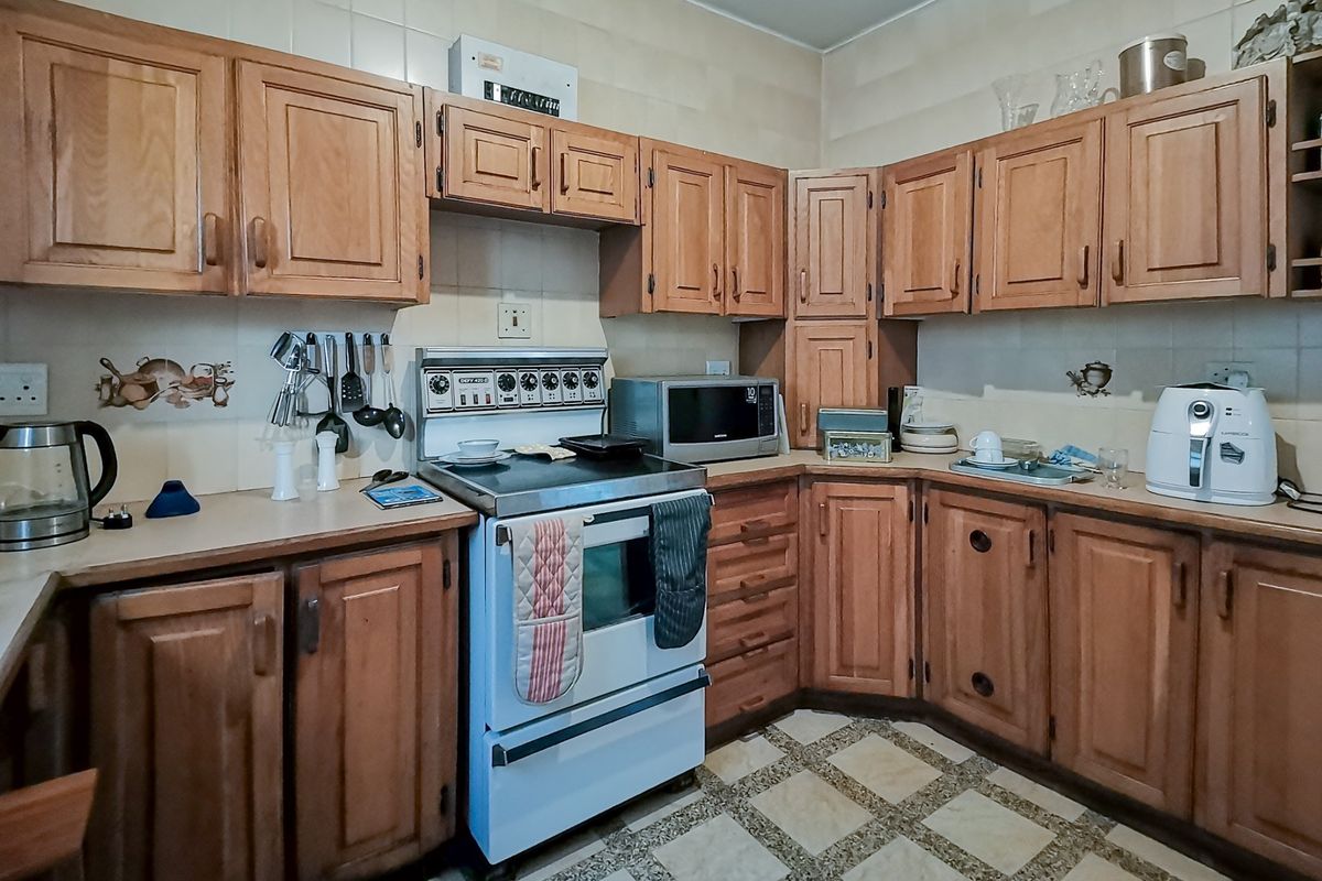 A functional kitchen featuring traditional wooden cabinetry, laminate countertops, a freestanding stove, and tiled flooring, offering a classic layout with potential for modernization.