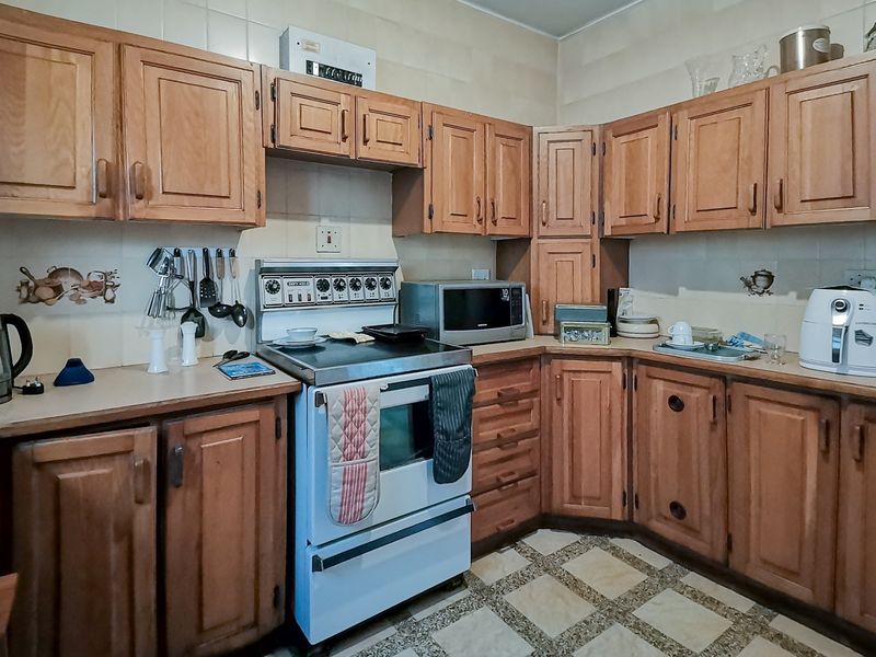 A functional kitchen featuring traditional wooden cabinetry, laminate countertops, a freestanding stove, and tiled flooring, offering a classic layout with potential for modernization.