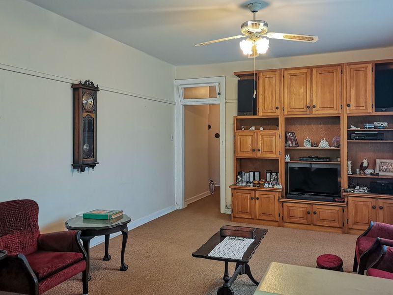A living room featuring built-in wooden cabinetry, a ceiling fan, and a transom window above the doorway, with carpeted flooring throughout.
