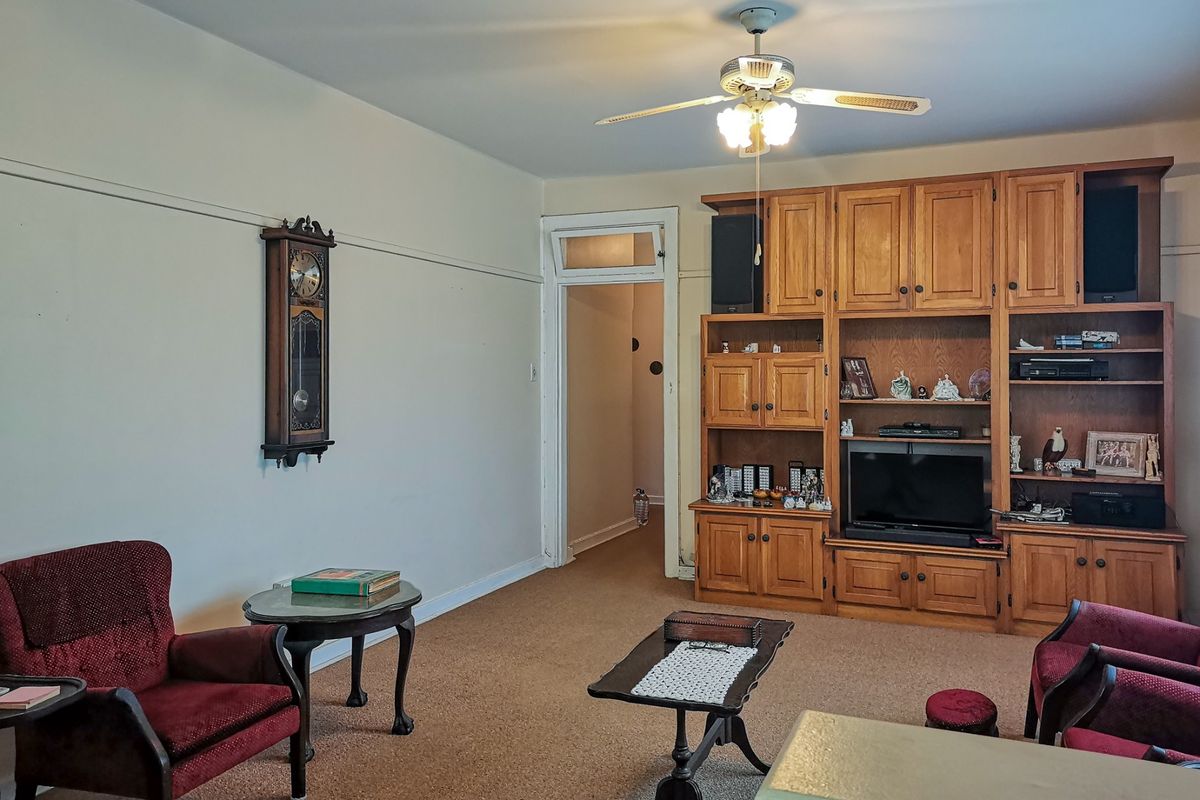 A living room featuring built-in wooden cabinetry, a ceiling fan, and a transom window above the doorway, with carpeted flooring throughout.