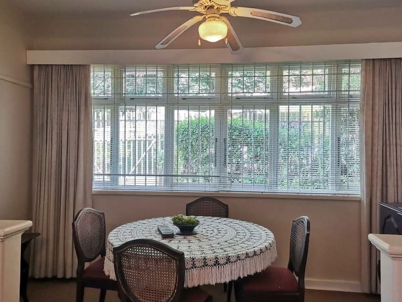 A dining area featuring a large multi-pane window with security bars, a ceiling fan, and neutral wall finishes.