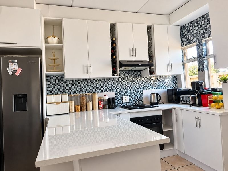 Modern kitchen featuring white cabinetry, quartz countertops, and a distinctive mosaic tile backsplash with integrated oven and hob.