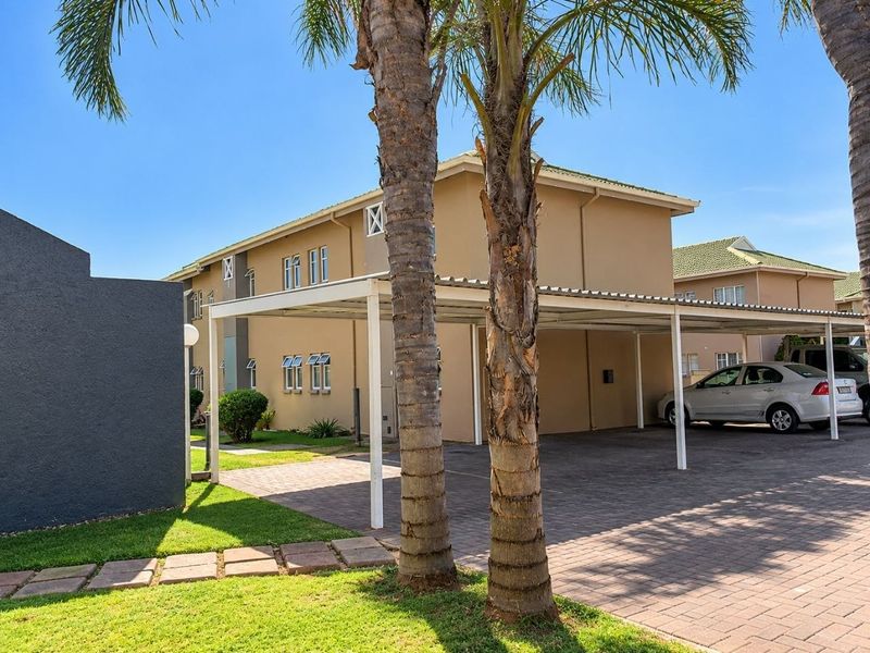 Exterior view of the apartment complex featuring a covered carport, paved driveway, and well-maintained garden area.