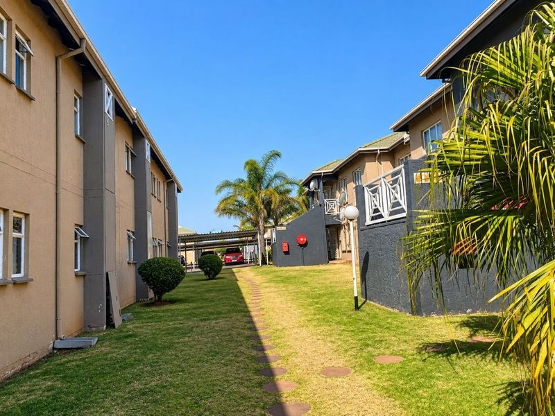 A view of the communal garden area between apartment blocks, featuring a paved walkway, manicured lawn, and exterior building finishes.