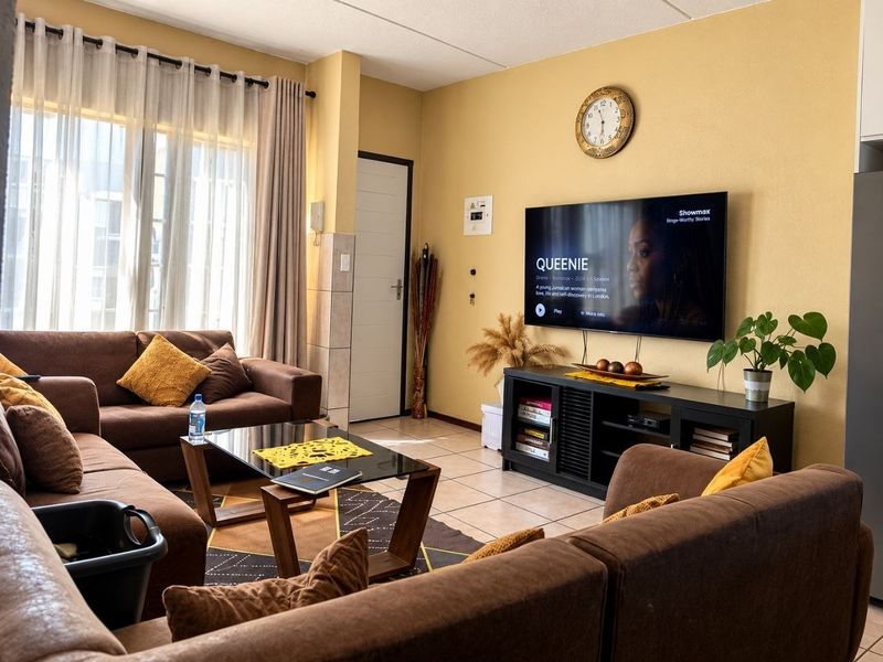 A comfortable living room featuring tiled flooring, neutral wall tones, and large windows with curtain treatments, providing a functional and well-lit space.