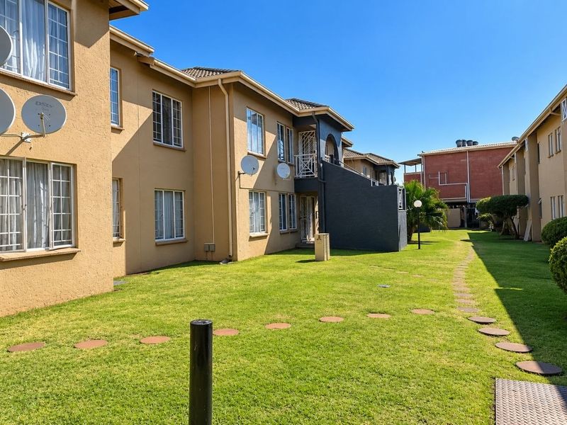 Exterior view of the apartment complex featuring a well-maintained lawn, stepping stone pathway, and multi-story residential units with external stair access.