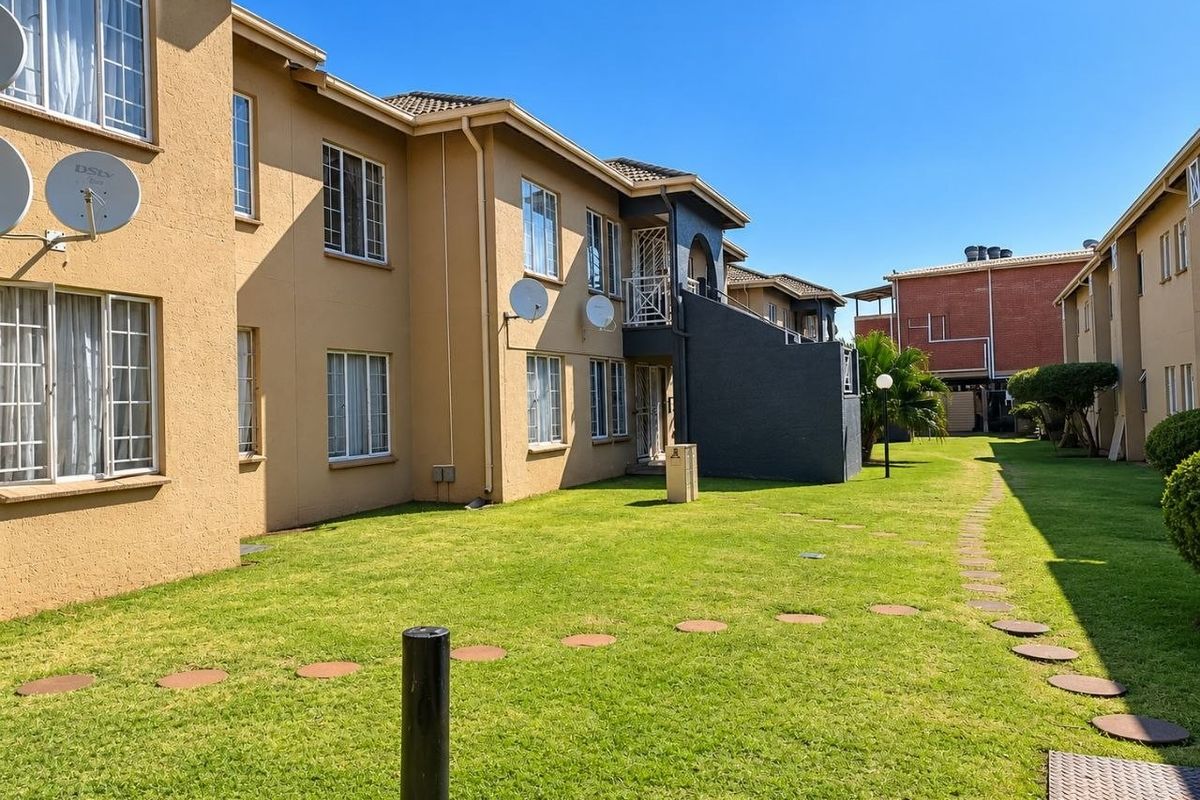 Exterior view of the apartment complex featuring a well-maintained lawn, stepping stone pathway, and multi-story residential units with external stair access.