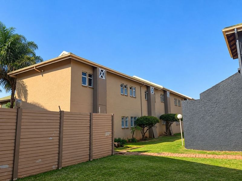 Exterior view of a multi-story apartment building featuring a plastered facade, sliding windows, and a well-maintained lawn with a paved walkway.