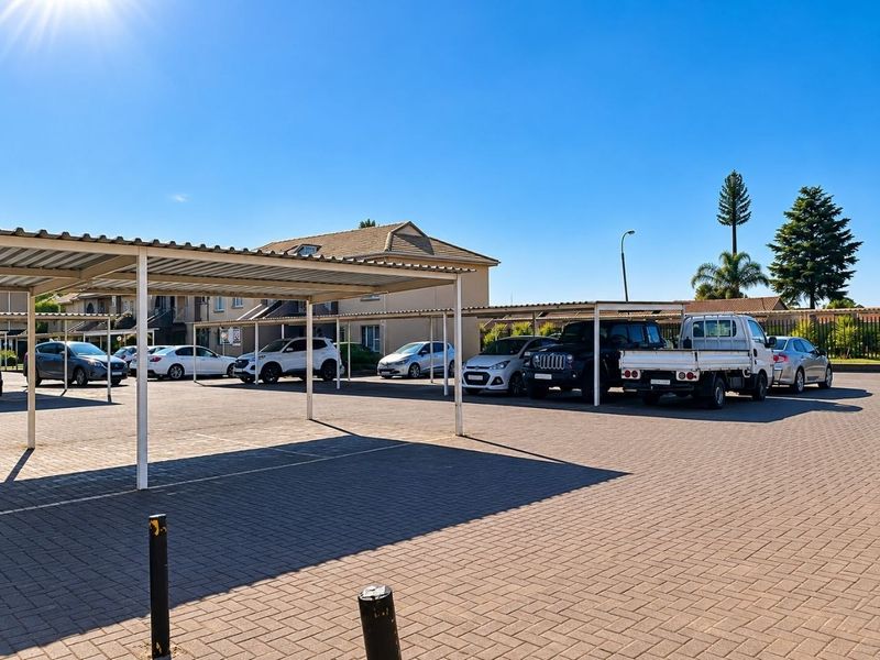 An open-air paved parking area featuring covered carport structures for resident vehicle storage within the apartment complex.