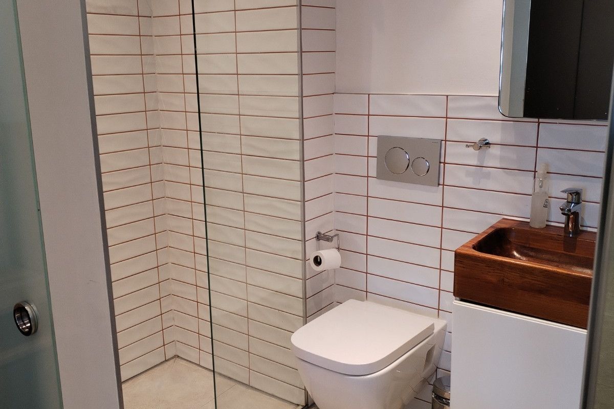 Modern bathroom featuring a wall-mounted toilet, walk-in shower with glass screen, and a vanity unit with a basin.