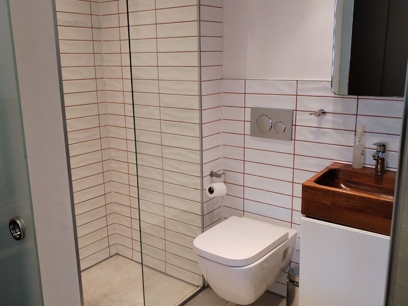 Modern bathroom featuring a wall-mounted toilet, walk-in shower with glass screen, and a vanity unit with a basin.