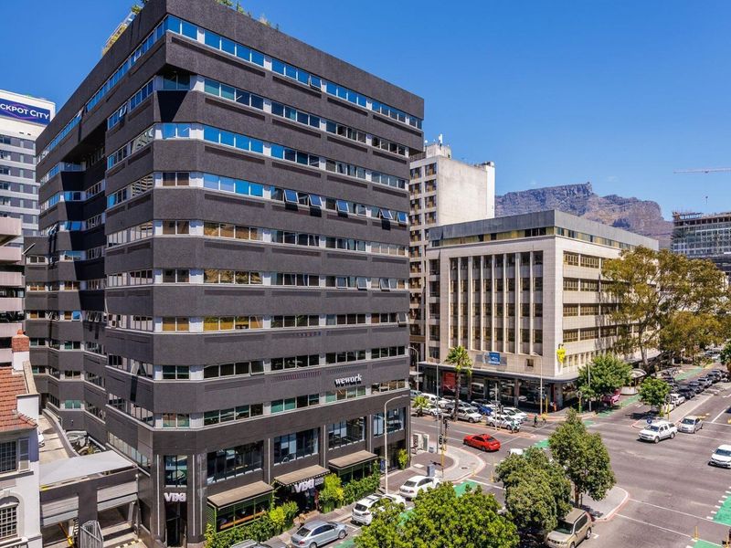 An elevated view of a modern multi-story commercial building situated on a busy urban street corner with mountain views in the background.