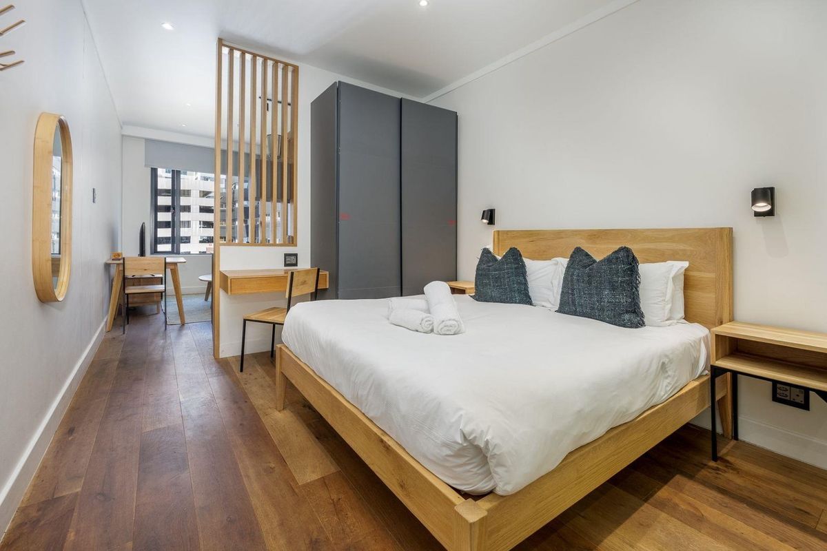 Modern bedroom featuring timber flooring, a built-in wardrobe, and a decorative timber room divider separating the sleeping area from a small workspace.