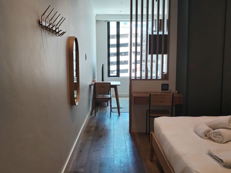 A modern bedroom featuring timber flooring, a built-in wardrobe, and a stylish timber slat divider creating a dedicated workspace area.