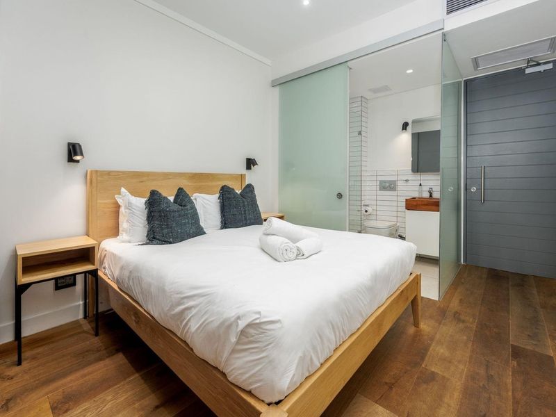 Modern bedroom featuring hardwood flooring, recessed lighting, and a sleek en-suite bathroom separated by a sliding glass door.