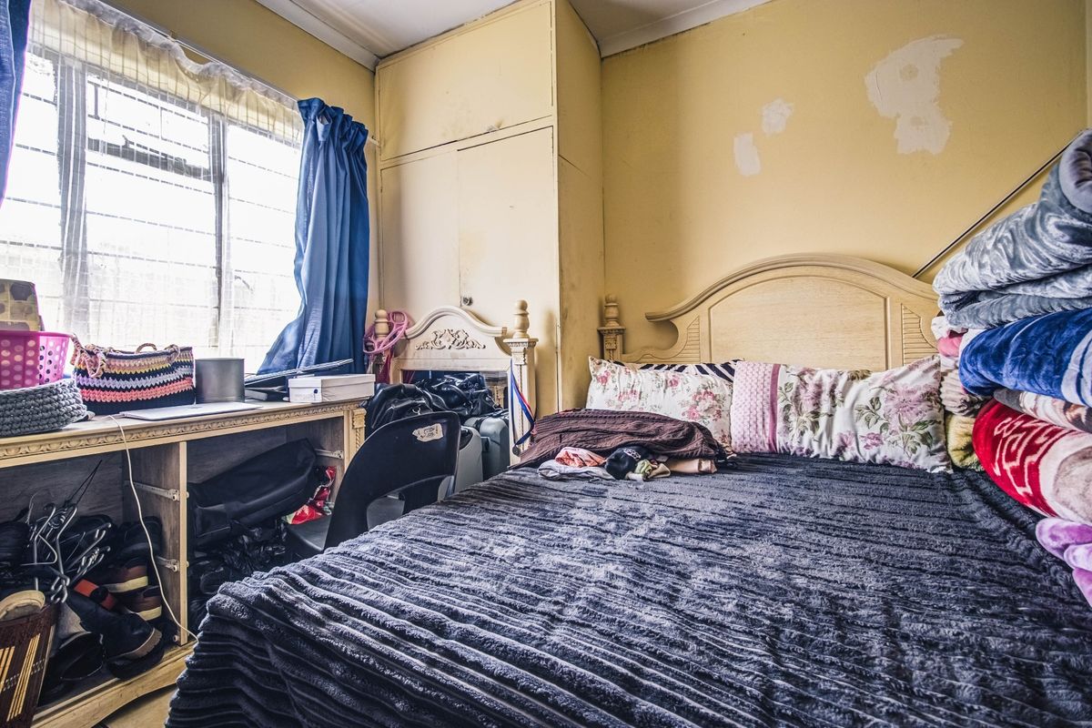 A bedroom featuring a built-in wardrobe and steel-framed window, currently requiring cosmetic updates to the wall finishes.