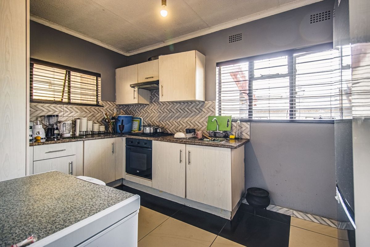 A functional kitchen featuring built-in cabinetry, a built-in oven with extractor fan, tiled backsplash, and tiled flooring with dual windows for natural light.