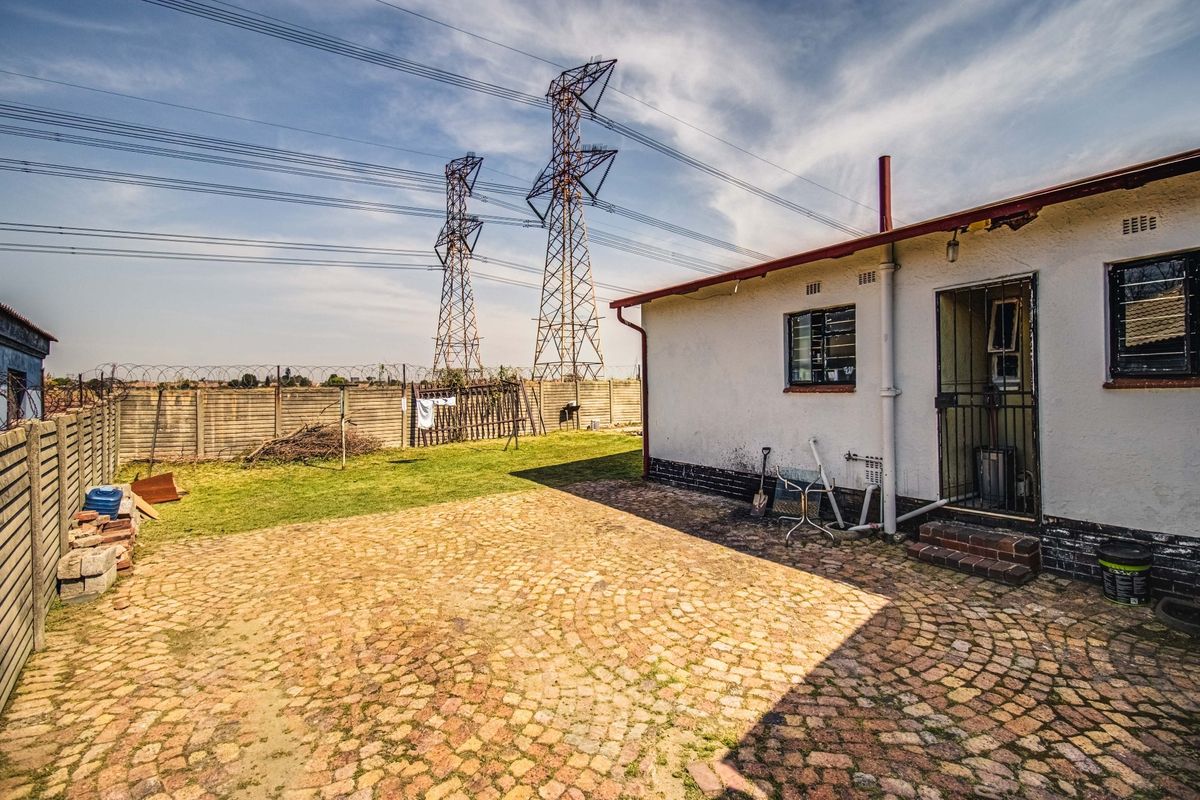 Rear exterior view featuring a cobblestone paved patio, lawn area, and precast concrete boundary wall with security fencing.