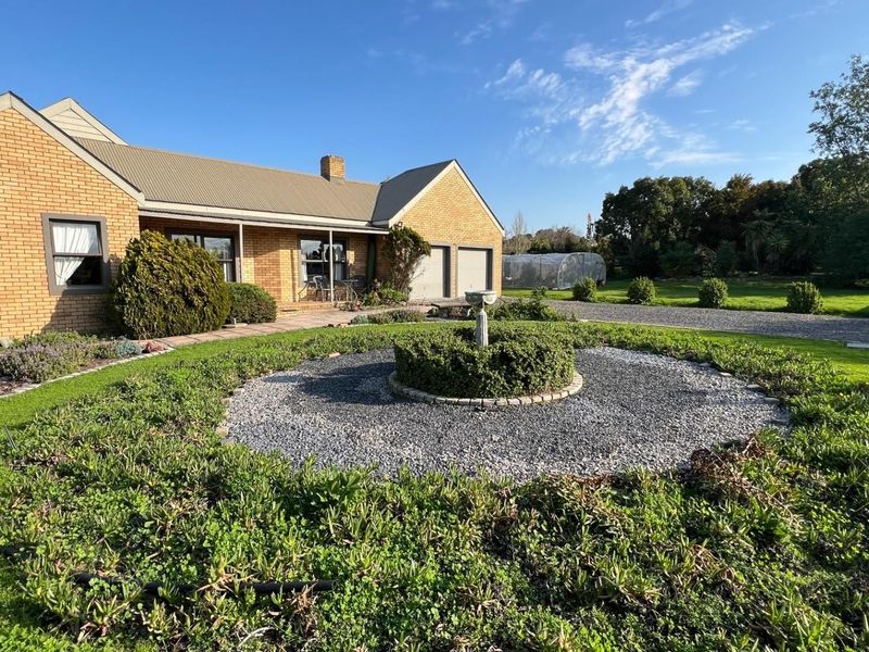 A well-maintained single-story brick house featuring a double garage, metal roof, and a landscaped front garden with a central stone fountain.