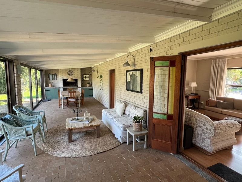 Spacious covered patio featuring brick flooring, exposed brick walls, and a built-in braai, seamlessly connecting to the interior living area through sliding doors.