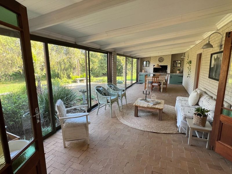 Spacious covered patio featuring brick flooring, built-in braai, and large sliding glass doors that open to the garden.