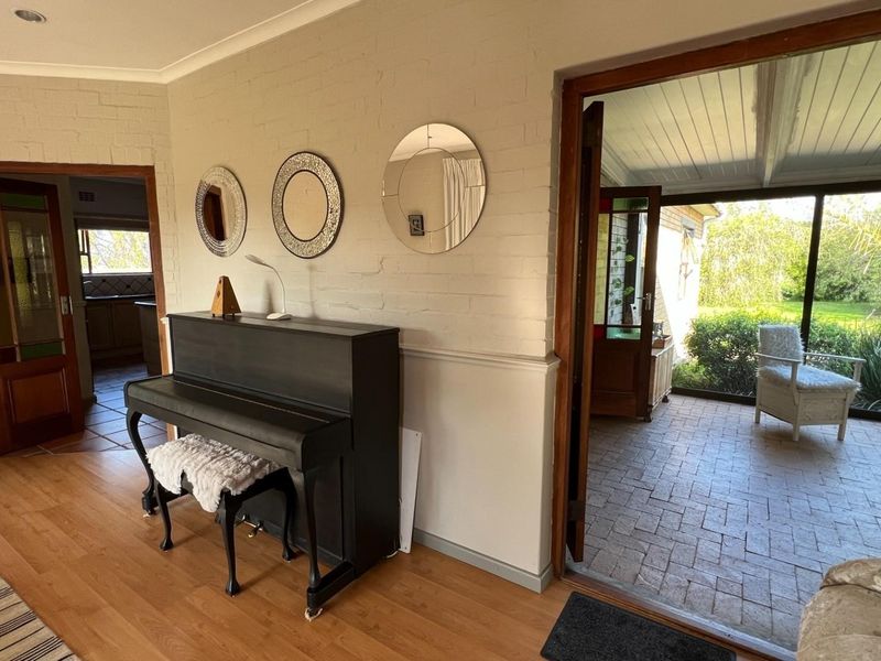 A bright living area featuring timber flooring, painted brick walls with wainscoting, and direct access to an outdoor patio space.