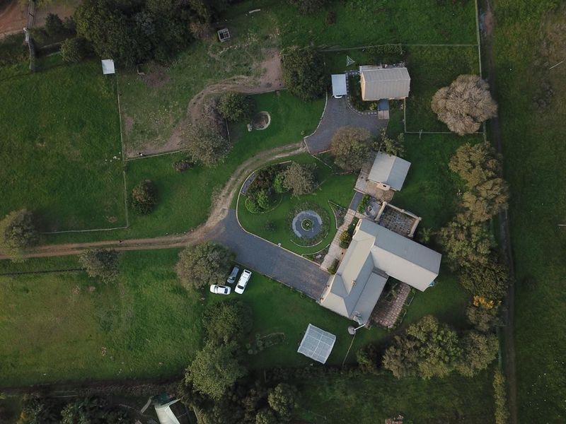 Aerial view of a large residential property featuring a main dwelling, multiple outbuildings, extensive landscaped gardens, and a paved driveway.