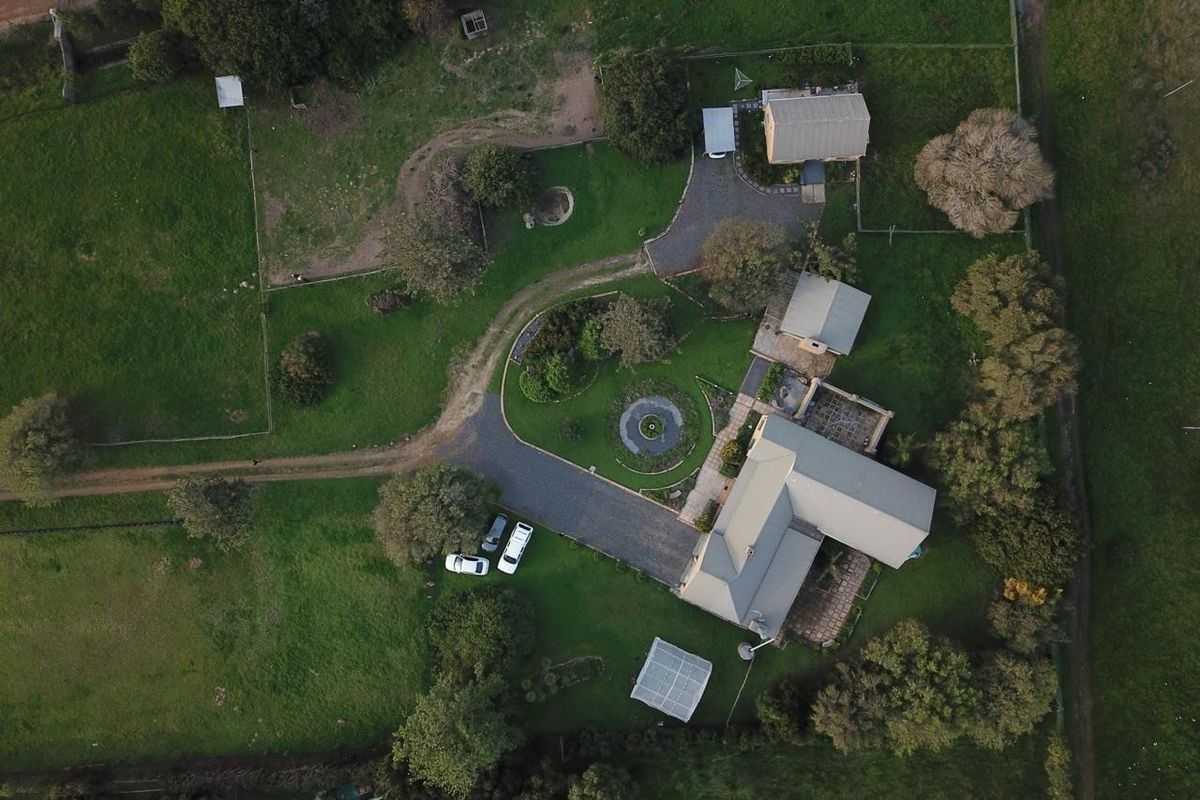 Aerial view of a large residential property featuring a main dwelling, multiple outbuildings, extensive landscaped gardens, and a paved driveway.