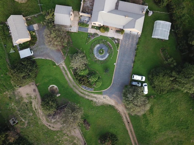 Aerial view of a residential property featuring a main house, outbuilding, greenhouse, landscaped garden, and a long gravel driveway.