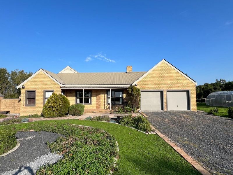 A well-maintained single-story brick house featuring a double garage, metal roof, and a landscaped front garden with a gravel driveway.