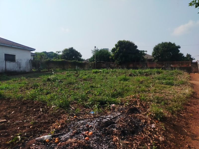 A vacant residential plot featuring perimeter fencing and boundary walls, currently covered in overgrown vegetation and surface debris.