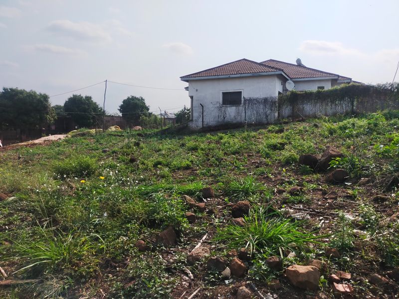 A view of the rear exterior of the property, featuring a sloped, undeveloped plot with overgrown vegetation and a residential building in the background.