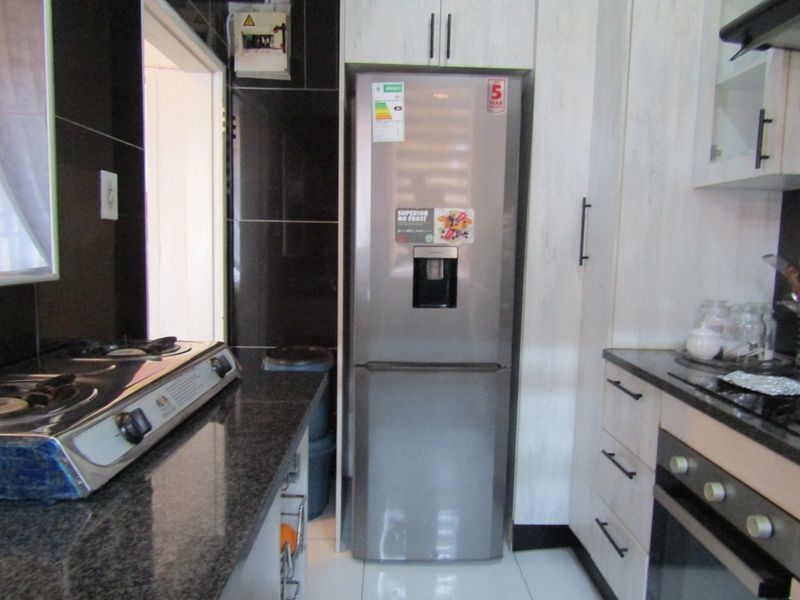 A functional kitchen featuring granite countertops, built-in cabinetry, a gas hob, and a built-in oven, with dark wall tiling and light floor tiles.