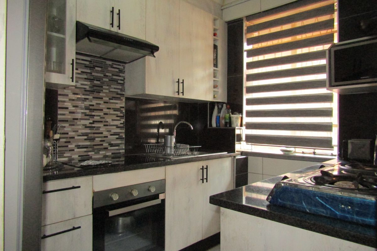 Modern kitchen featuring light wood-grain cabinetry, dark granite countertops, a mosaic tile backsplash, and integrated appliances including an oven and extractor fan.