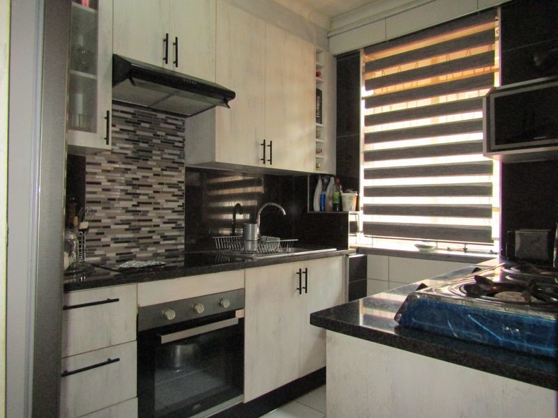 Modern kitchen featuring light wood-grain cabinetry, dark granite countertops, a mosaic tile backsplash, and integrated appliances including an oven and extractor fan.