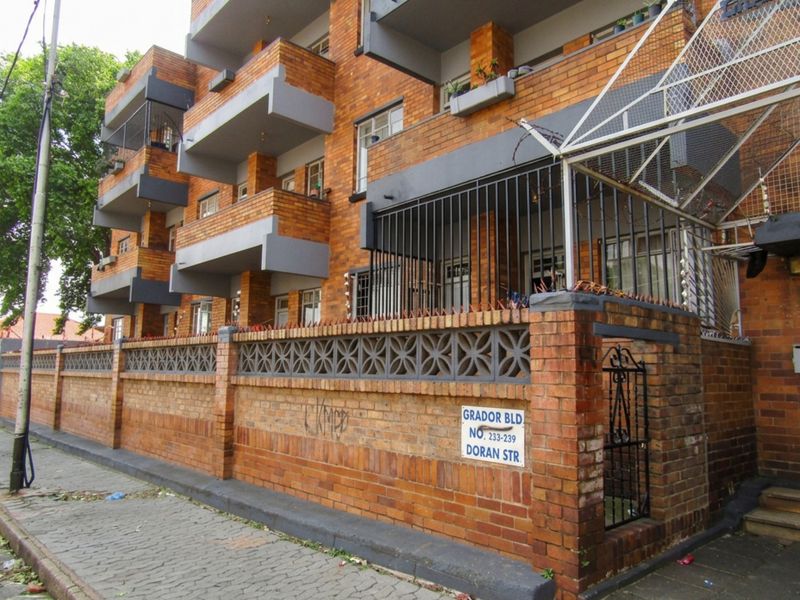 Exterior view of a multi-story brick apartment building featuring private balconies and a secure perimeter wall with metal fencing.